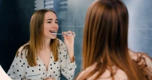 woman brushing her teeth in front of a mirror woman brushing her teeth in front of a mirror